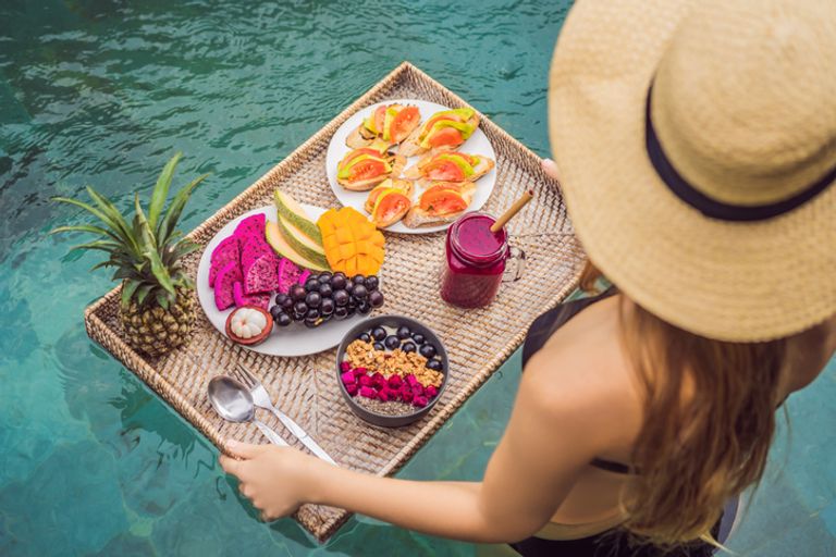 Breakfast Tray In Swimming Pool, Floating Breakfast In Luxury Hotel. Girl Relaxing In The Pool Drinking Smoothies And Eating Fruit Plate, Smoothie Bowl By The Hotel Pool. Exotic Summer Diet. Tropical Beach Lifestyle. Bali Trend